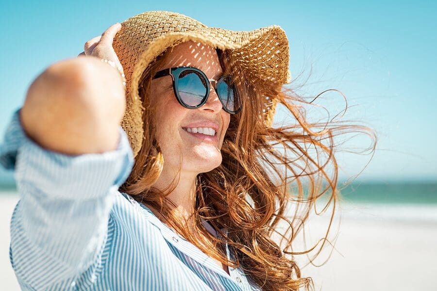 A woman with long hair wearing sunglasses and a hat.