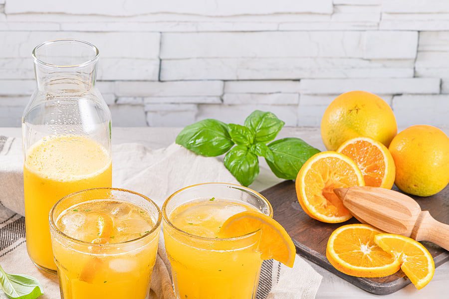 A table with two glasses of orange juice and some fruit.