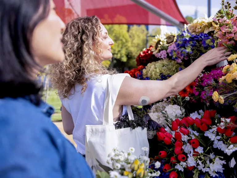Woman picking out flowers while wearing a Stelo glucose monitor on the back of her arm.