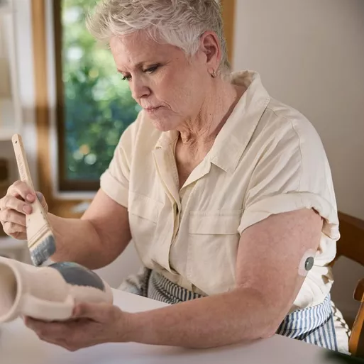 Woman painting pottery while wearing a Stelo glucose monitor