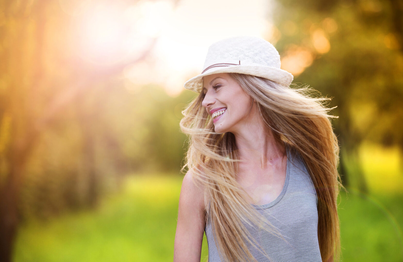 Attractive young woman, with long flowing hair, enjoying her time outside in park with sunset in background.