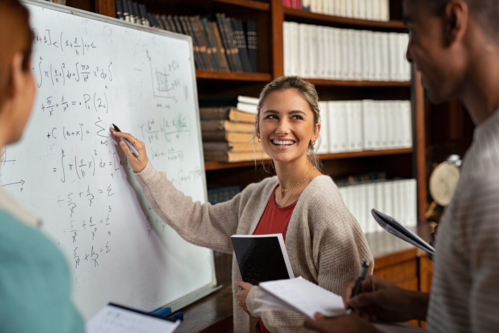 Happy college girl writing math formulas on whiteboard.