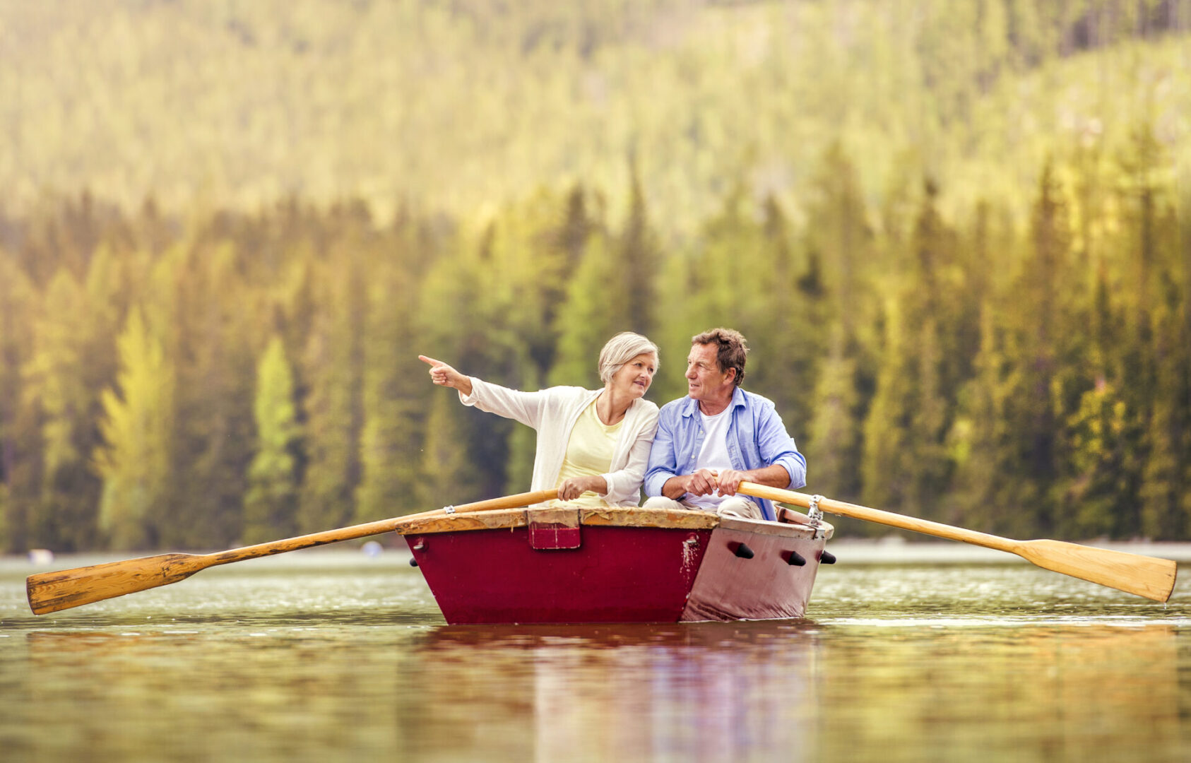 Senior couple paddling on boat with mountains in background