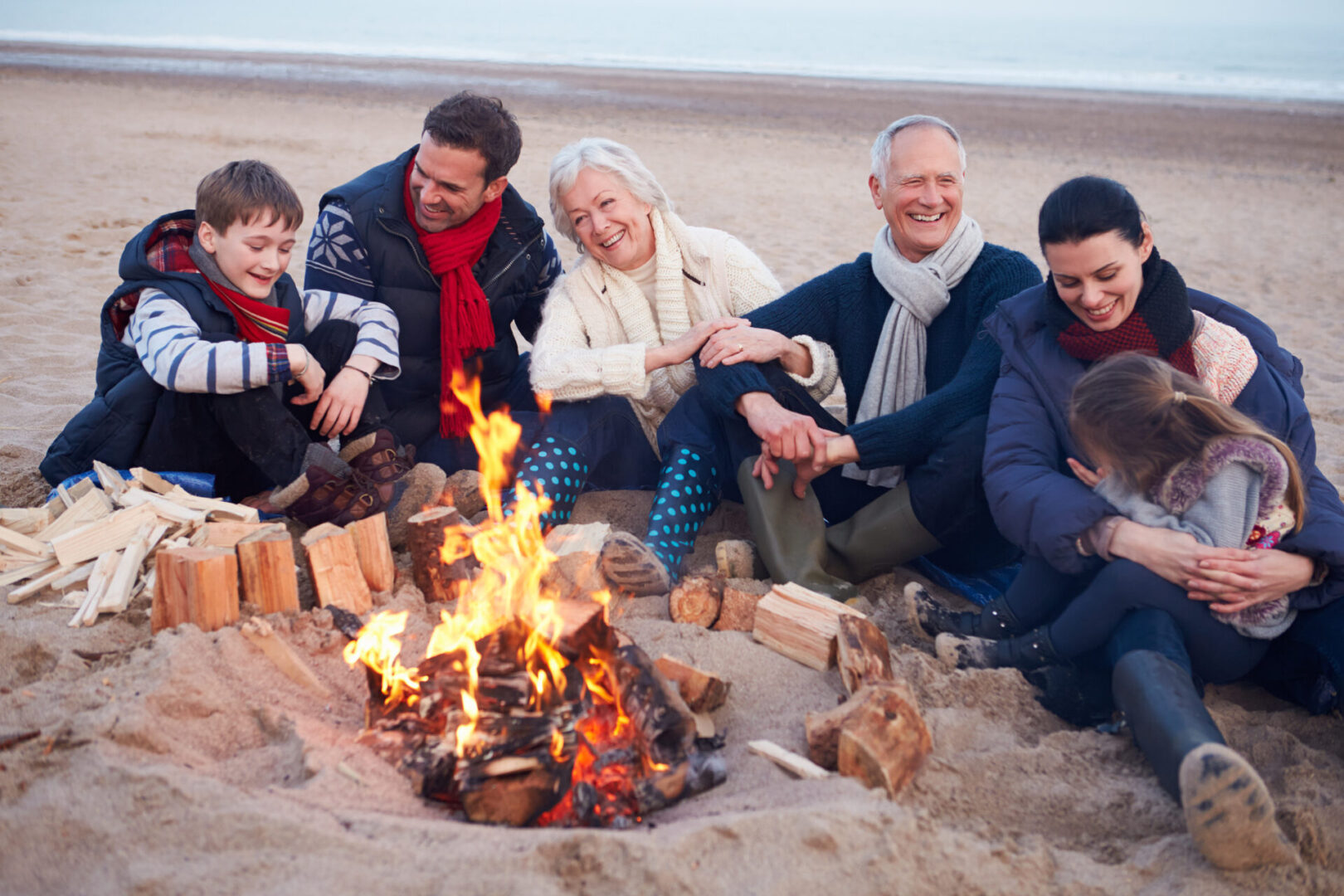 Multi Generation Family Sitting By Fire On Winter Beach Representing boosted immune systems close to family