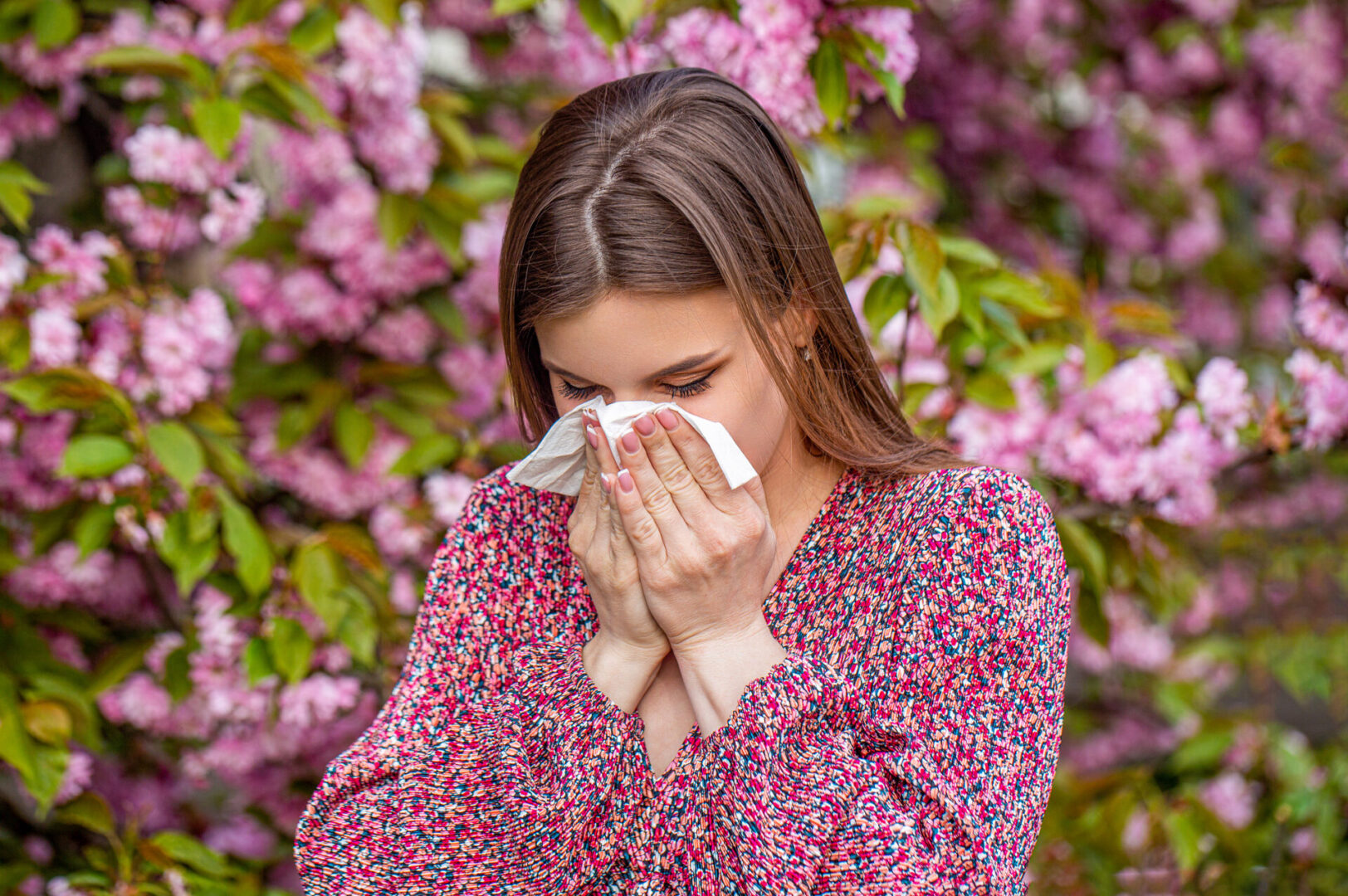 Woman sneezing in front of pink flowered tree representing gut health and allergies