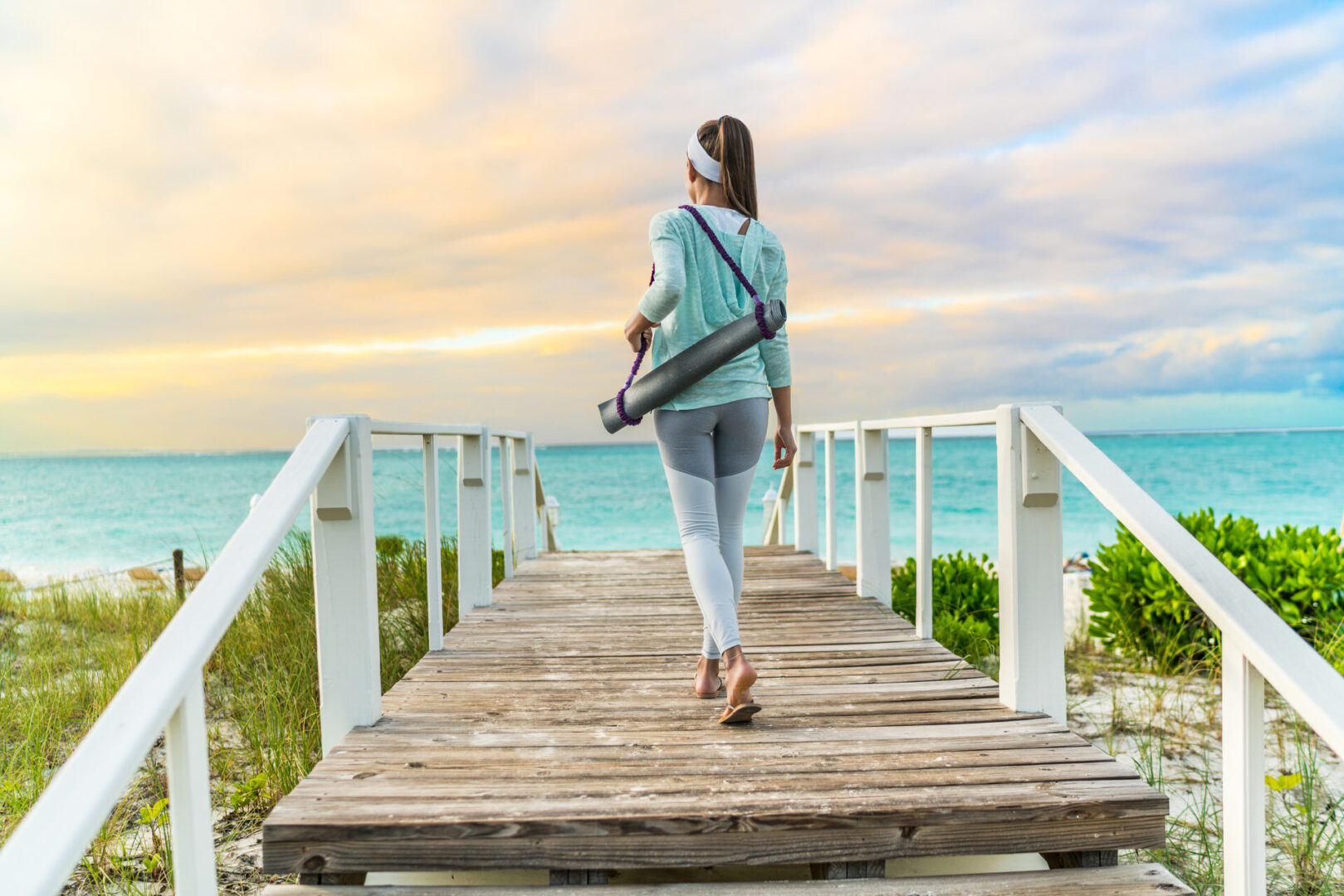 Woman walking to beach on a boardwalk carrying yoga mat for healthy methylation