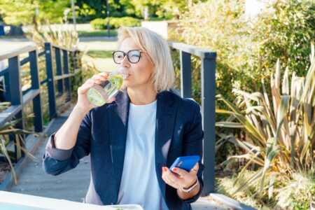 Woman drinking electrolytes for everyday health while walking through the park.