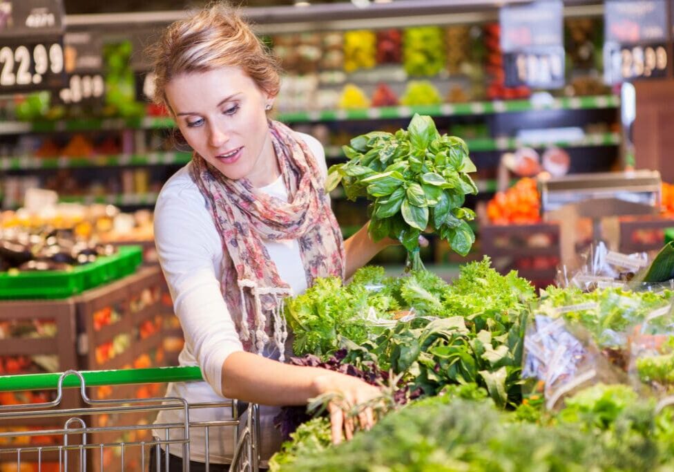 Portrait of beautiful young woman choosing green leafy vegetables in grocery store. Concept of healthy food shopping