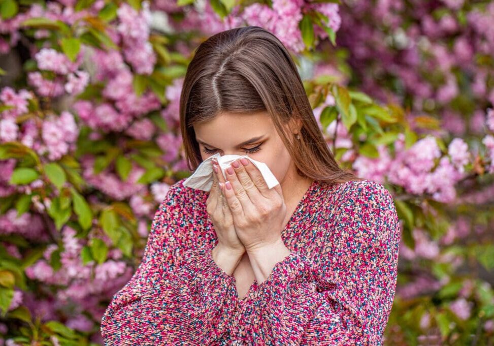 Woman sneezing in front of pink flowered tree representing gut health and allergies