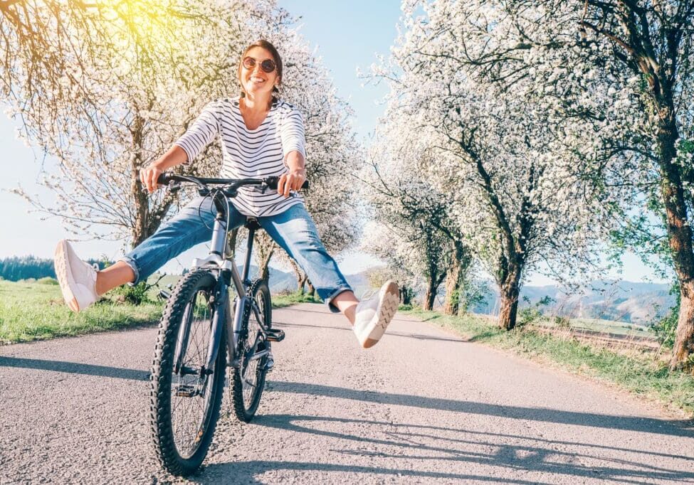 Woman riding a bike in the spring with flowery trees all around, with a healthy immune system.