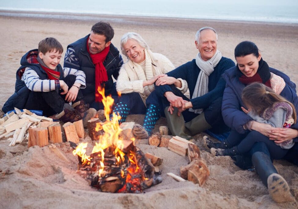 Multi Generation Family Sitting By Fire On Winter Beach Representing boosted immune systems close to family