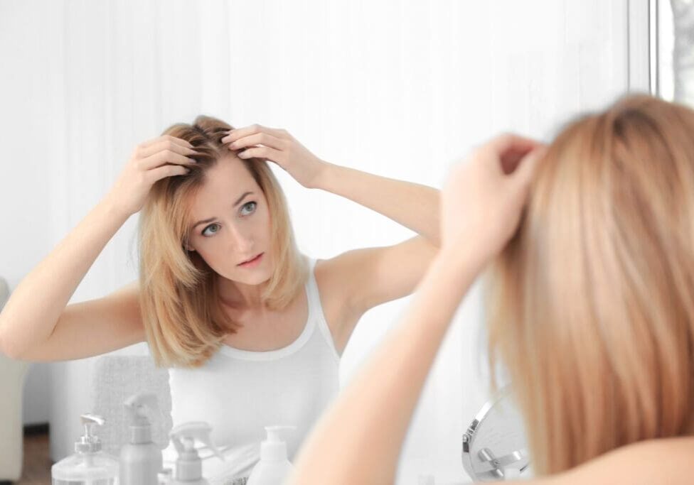 Young woman with hair loss problem looking in mirror at home Young woman with hair loss problem looking in mirror at home