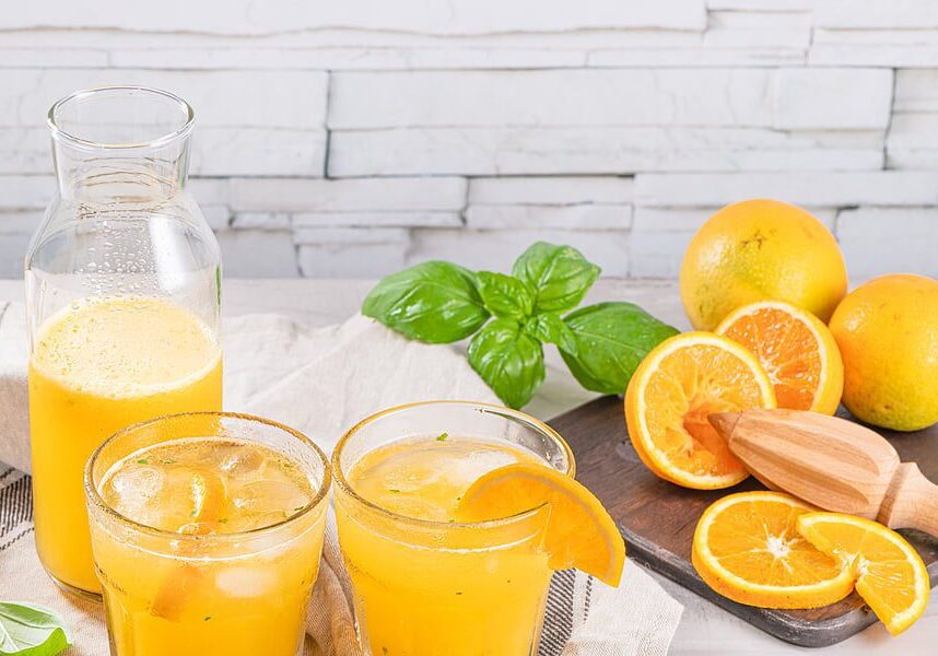 A table with two glasses of orange juice and some fruit.